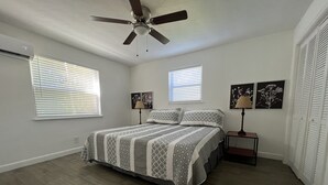 A bedroom with a bed, two bedside tables, a ceiling fan, and two windows with blinds. - Spacious one-bedroom beach apartment on Singer Island (Palm Beach Shores)