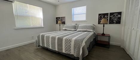 A bedroom with a bed, two bedside tables, a ceiling fan, and two windows with blinds.