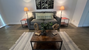 A living room with a grey sofa, two side tables with lamps, a coffee table with decorative items, and a patterned rug. - Spacious one-bedroom beach apartment on Singer Island (Palm Beach Shores)