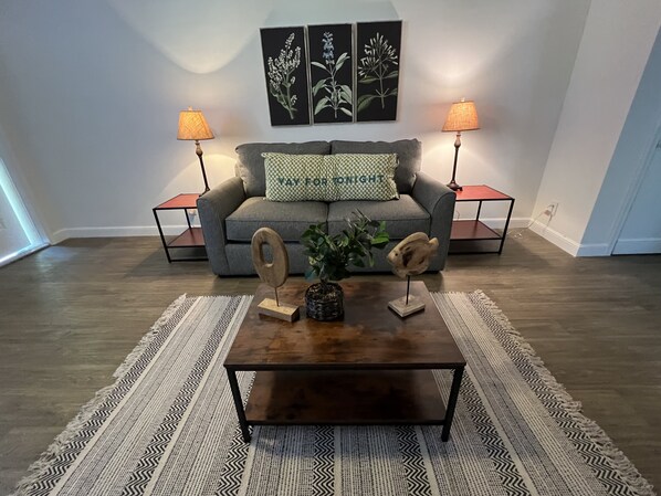 A living room with a grey sofa, two side tables with lamps, a coffee table with decorative items, and a patterned rug.