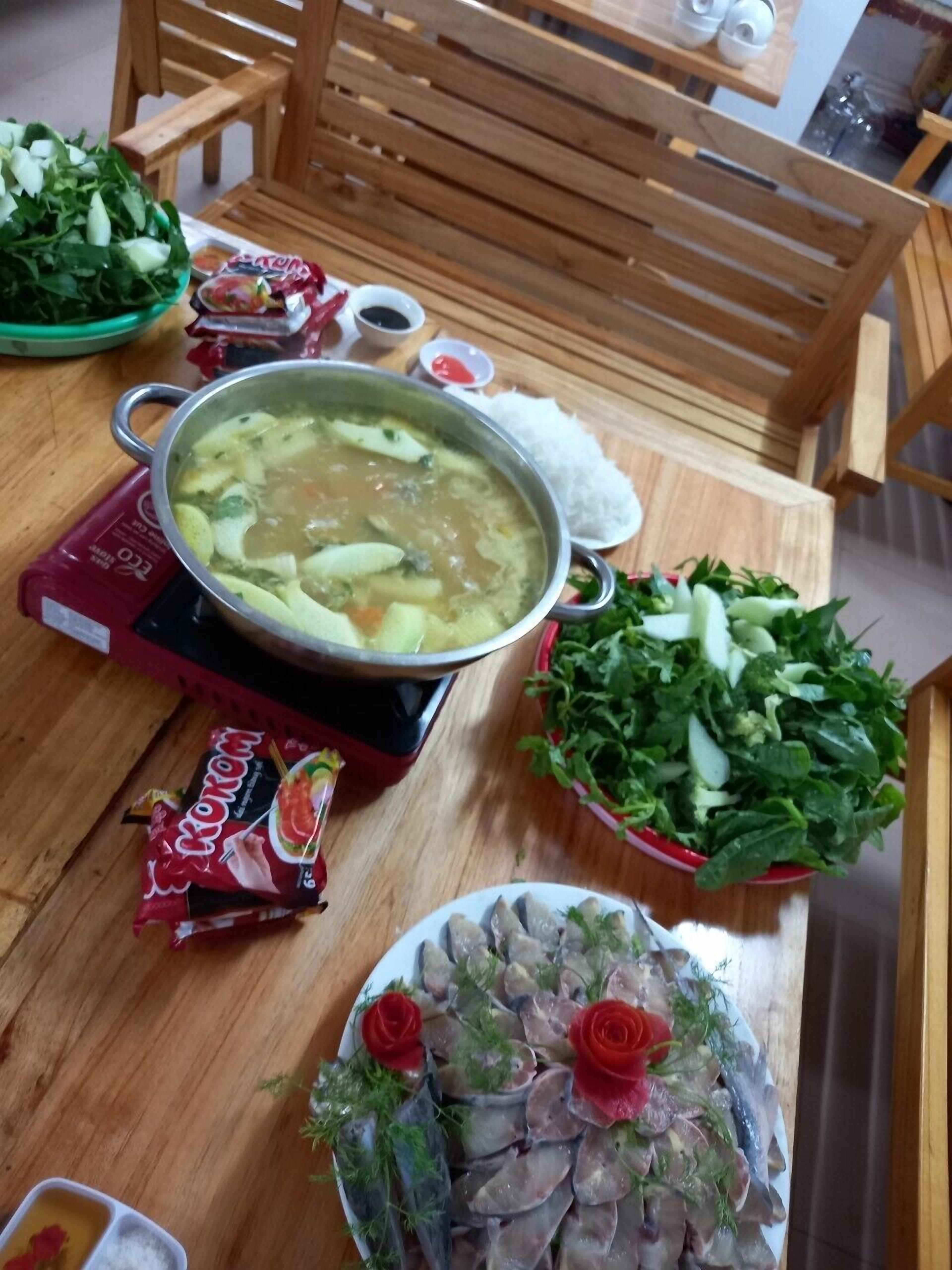 A table with a pot of soup, a bowl of greens, a plate of fish, and condiments.