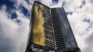 A tall, modern skyscraper with a curved facade, featuring a mix of reflective and dark glass windows. - Luxurious 1 Bdrm Apartment in GC Casino (Broadbeach)