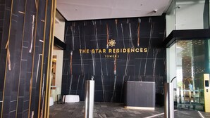 A modern reception area with a dark marble wall, a glass elevator, and a reception desk. - Luxurious 1 Bdrm Apartment in GC Casino (Broadbeach)
