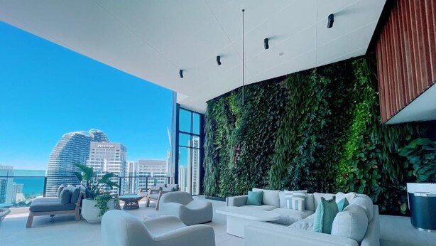 A modern living room with white sofas and a green vertical garden wall. - Luxurious 1 Bdrm Apartment in GC Casino (Broadbeach)