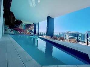 Relax by the pool with a clear view of the city skyline, surrounded by lounge chairs and a bench.