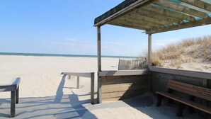 A beachside wooden structure with benches and a covered area, overlooking a sandy beach and ocean.