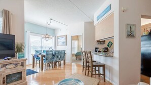 A modern living room with a TV, dining area, kitchen, and a view of the outdoors.