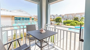 A balcony with a table and chairs, overlooking a swimming pool and neighboring houses.