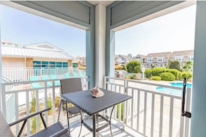 Een balkon met een tafel en stoelen, met uitzicht op een zwembad en omliggende huizen.
