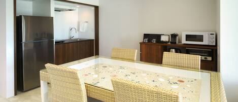 A compact kitchen with a refrigerator, microwave, and coffee maker. There is a glass-top table with wicker chairs.