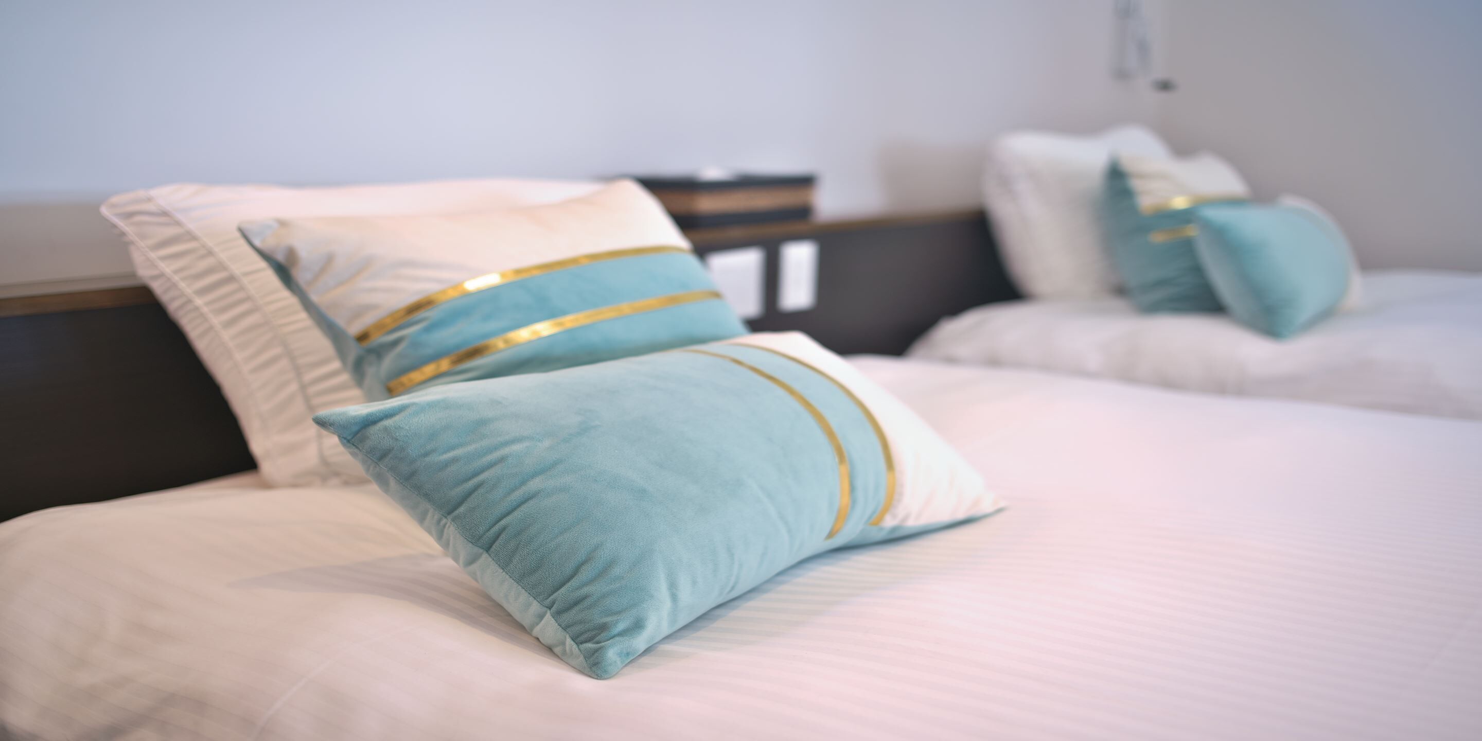 A neatly made bed with two pillows, one with a gold stripe.