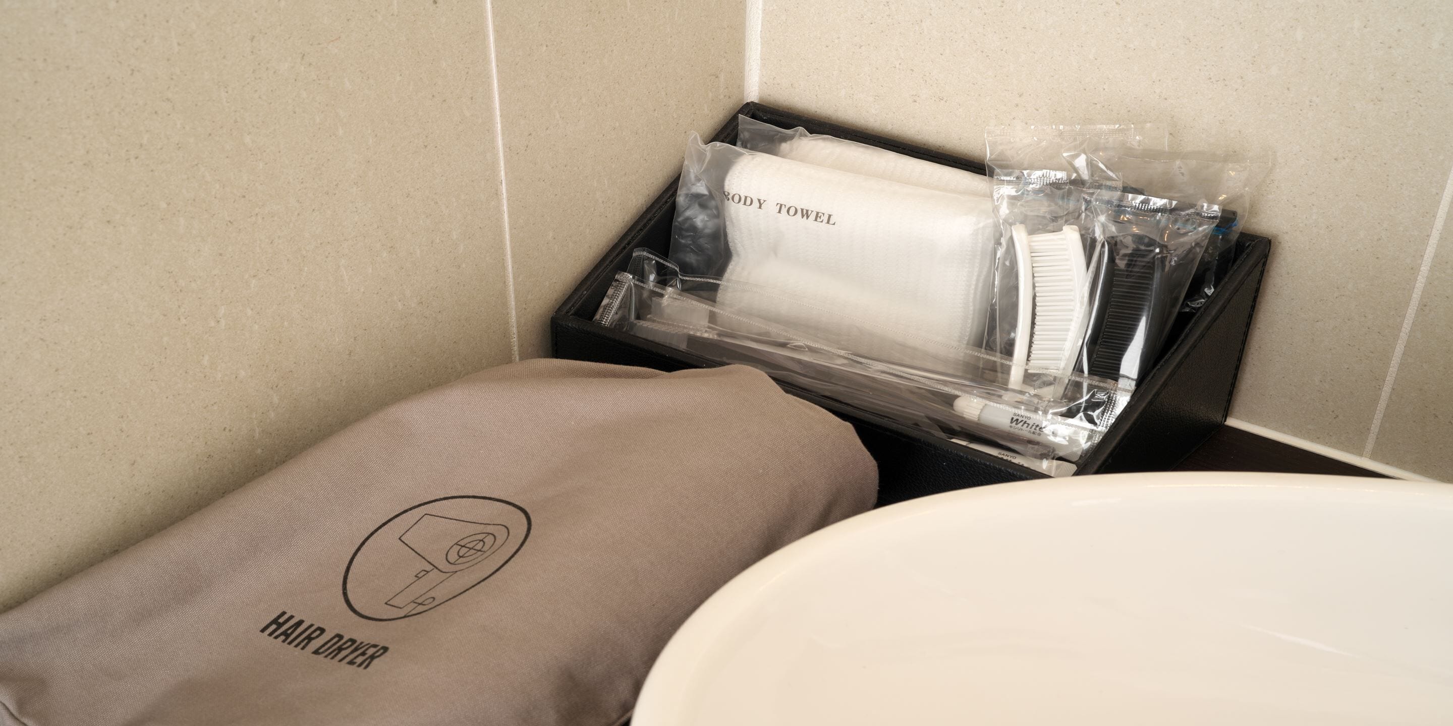 Un baño con una toalla color beige, una toalla de cuerpo blanca y un secador de pelo en una bandeja negra.
