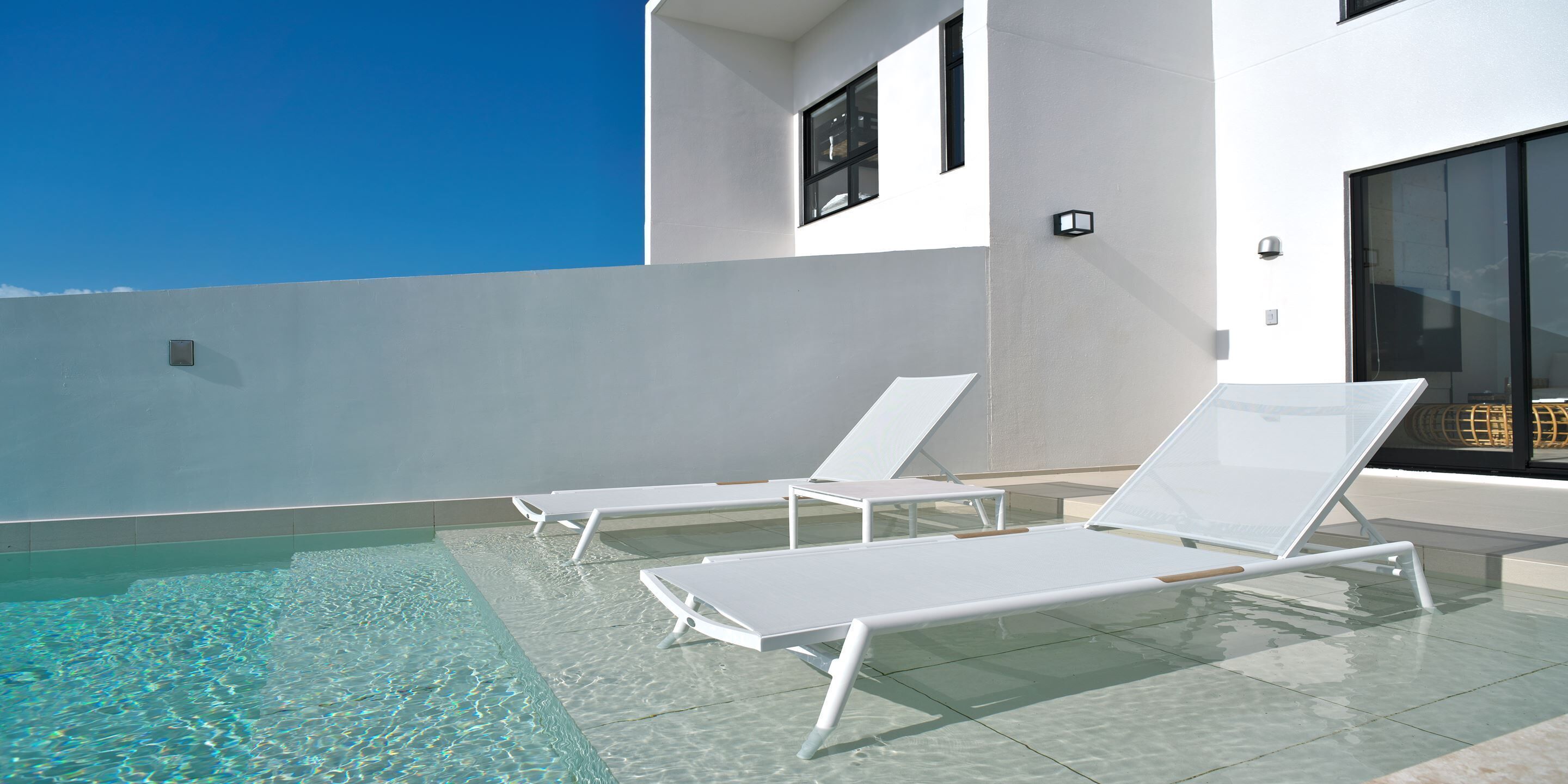 A rooftop pool area with two white lounge chairs and a clear blue sky.