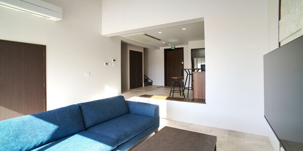 A modern living room with a blue sofa, a coffee table, and a staircase leading to an upper floor. - ADANRESORT LANA Villa Suite (Motobu)
