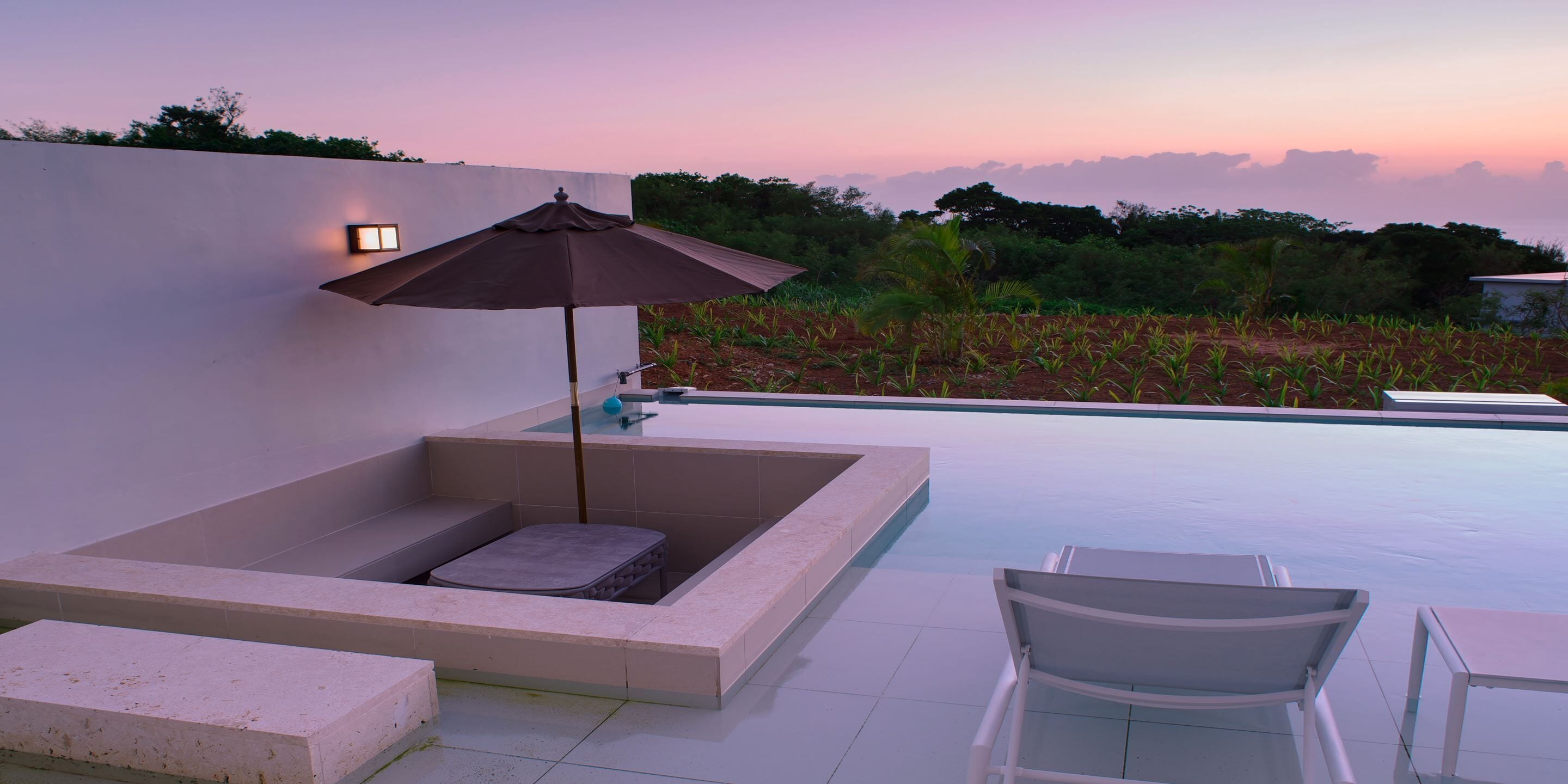 Un área de piscina moderna al aire libre con una zona de estar integrada, una silla de descanso y una mesa.