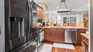 A modern kitchen with stainless steel appliances, wooden cabinets, and a large window providing natural light. - Luxurious home with golf course view, deck, grill, Peloton! King size bed.  (Fairfax)