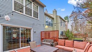 A patio with a wooden table and chairs, a wicker sofa, and a lattice screen. - Luxurious home with golf course view, deck, grill, Peloton! King size bed.  (Fairfax)