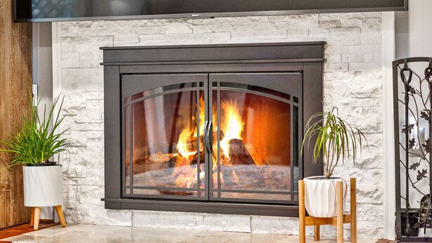 A modern fireplace with a stone wall backdrop, flanked by potted plants. - Luxurious home with golf course view, deck, grill, Peloton! King size bed.  (Fairfax)