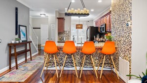 A modern kitchen with a tiled backsplash, wooden cabinets, and a central island with orange bar stools. - Luxurious home with golf course view, deck, grill, Peloton! King size bed.  (Fairfax)