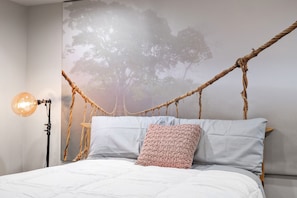 Ein Bett mit Kordelstirnbrett, einer Pendelleuchte und Wandmalerei.