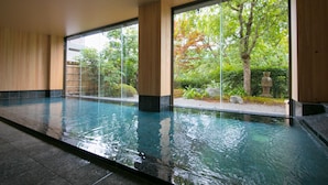 A large indoor swimming pool with clear glass walls, surrounded by wooden paneling and a view of trees and greenery outside. - Fukiya Ryokan (Yugawara)