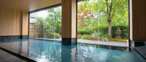 Una amplia piscina interior con paredes de vidrio transparente, rodeada de paneles de madera y vistas a árboles y vegetación.