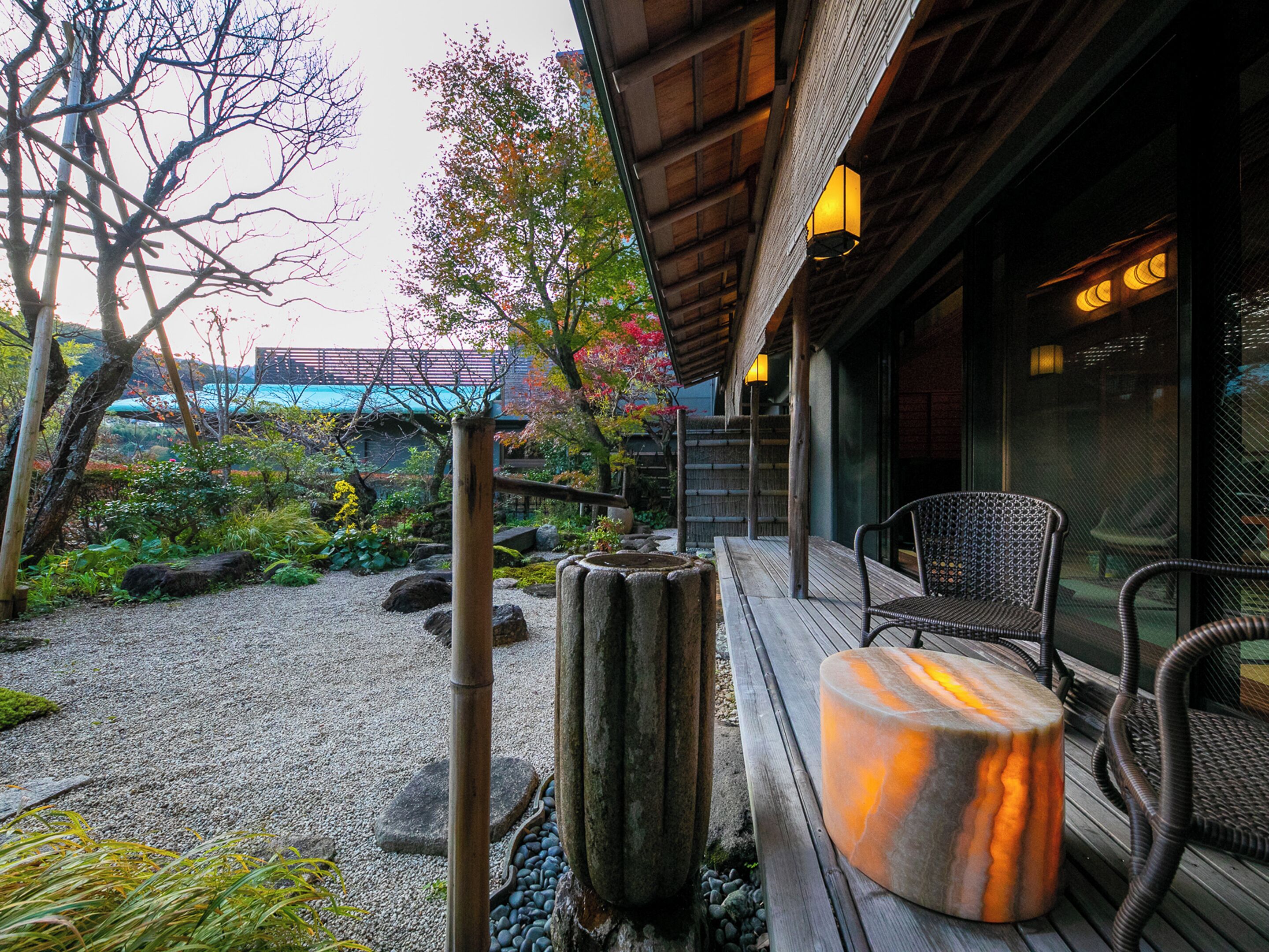 A traditional Japanese garden with a wooden deck, stone lantern, and a view of a building in the background.