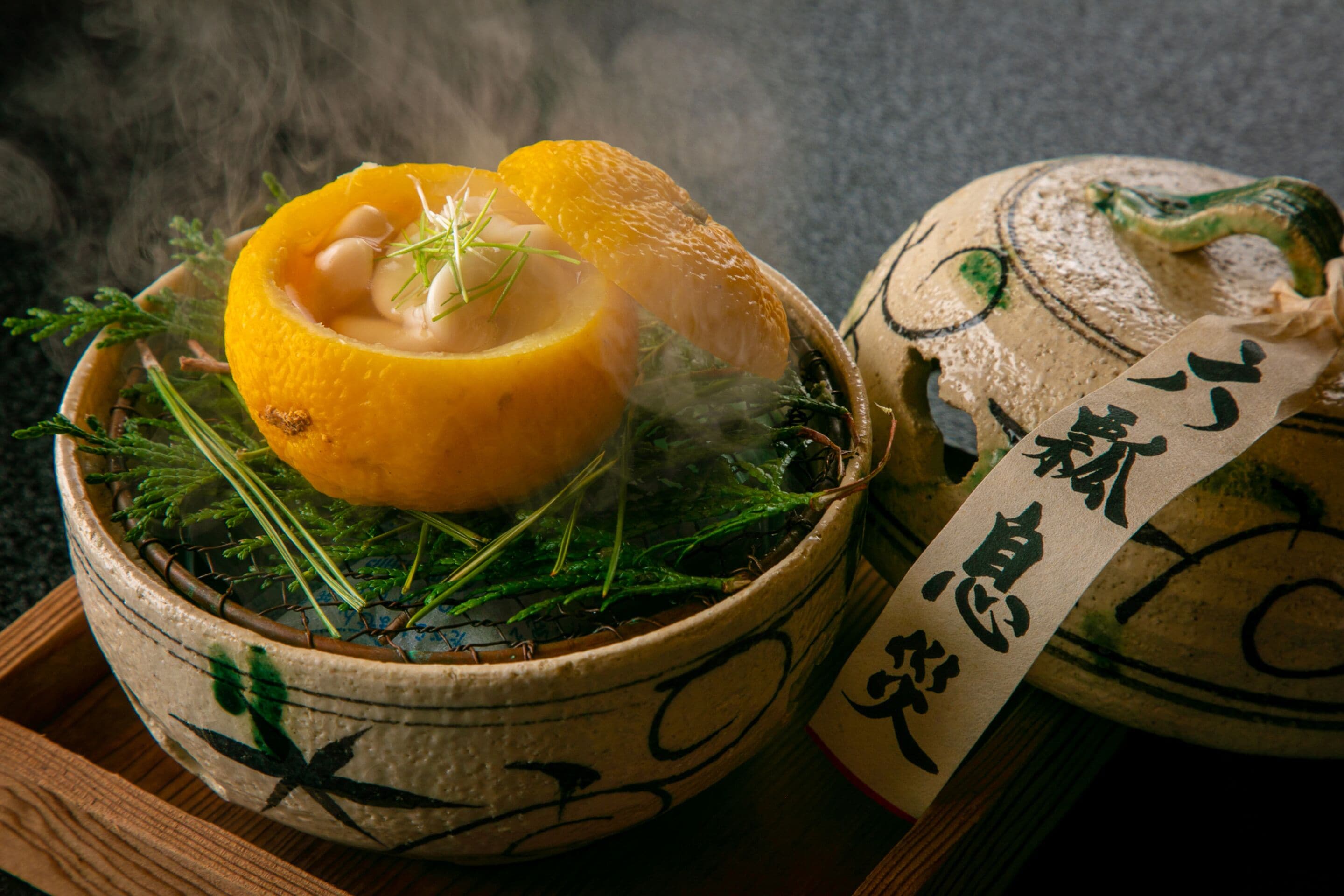 Egy hagyományos japán étel, mely egy tálban van tálalva, és tartalmaz faragott narancssárga és zöld zöldségeket, a gőz felfelé árad, és egy japán írásjegyekkel díszített papír kíséri.