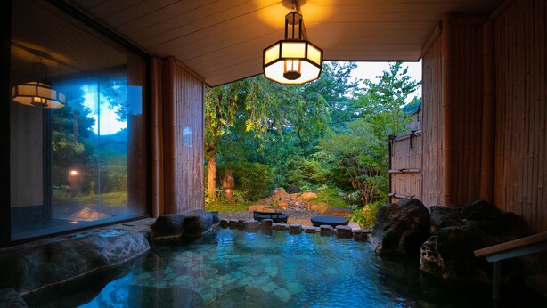 A hot spring area with a wooden deck, stone seating, and a view of a forested landscape. - Fukiya Ryokan (Yugawara)