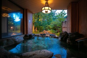 A hot spring area with a wooden deck, stone seating, and a view of a forested landscape. - Fukiya Ryokan (Yugawara)