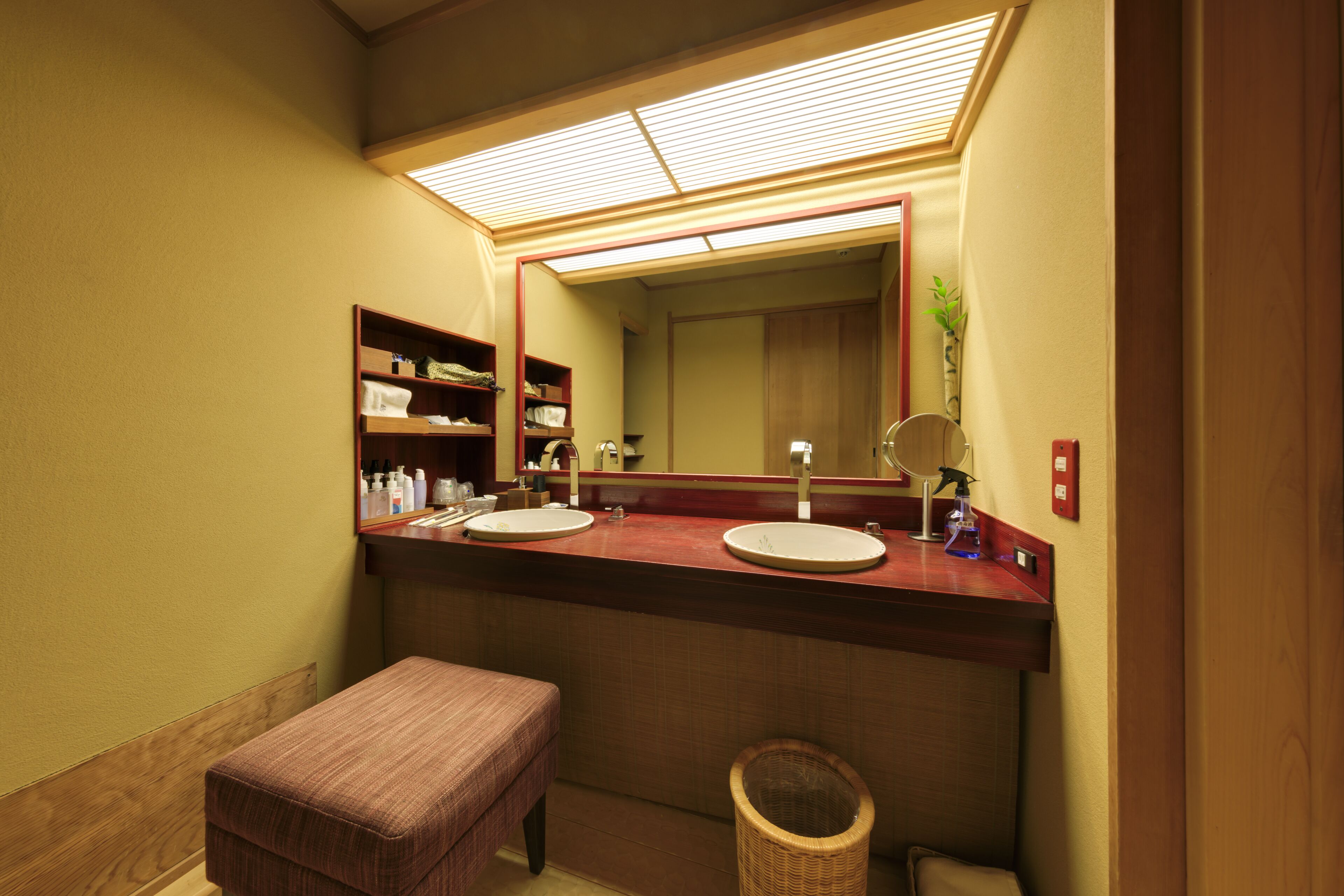 A bathroom with two sinks, a mirror, shelves with toiletries, and a bench.