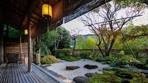 A wooden deck with a seating area, a stone pathway, and a view of a garden with rocks and moss. - Fukiya Ryokan (Yugawara)