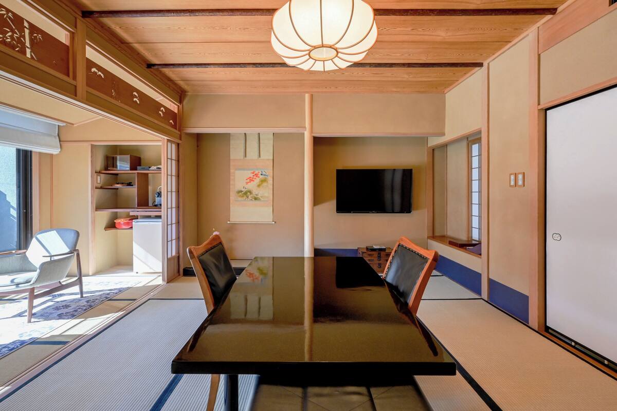 A traditional Japanese-style room with tatami flooring, a low table, and a television mounted on the wall.