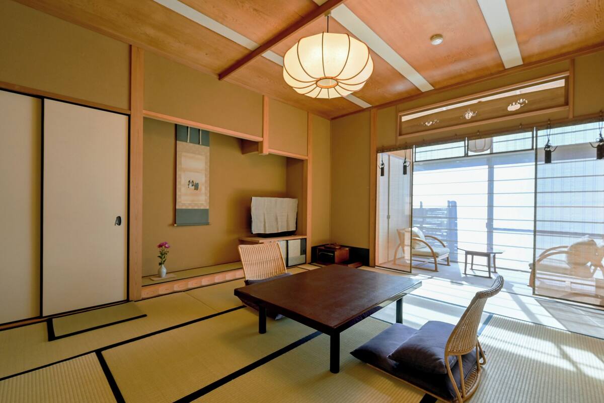 A traditional Japanese room with tatami flooring, a low table, a sofa, and a sliding door leading to a balcony.