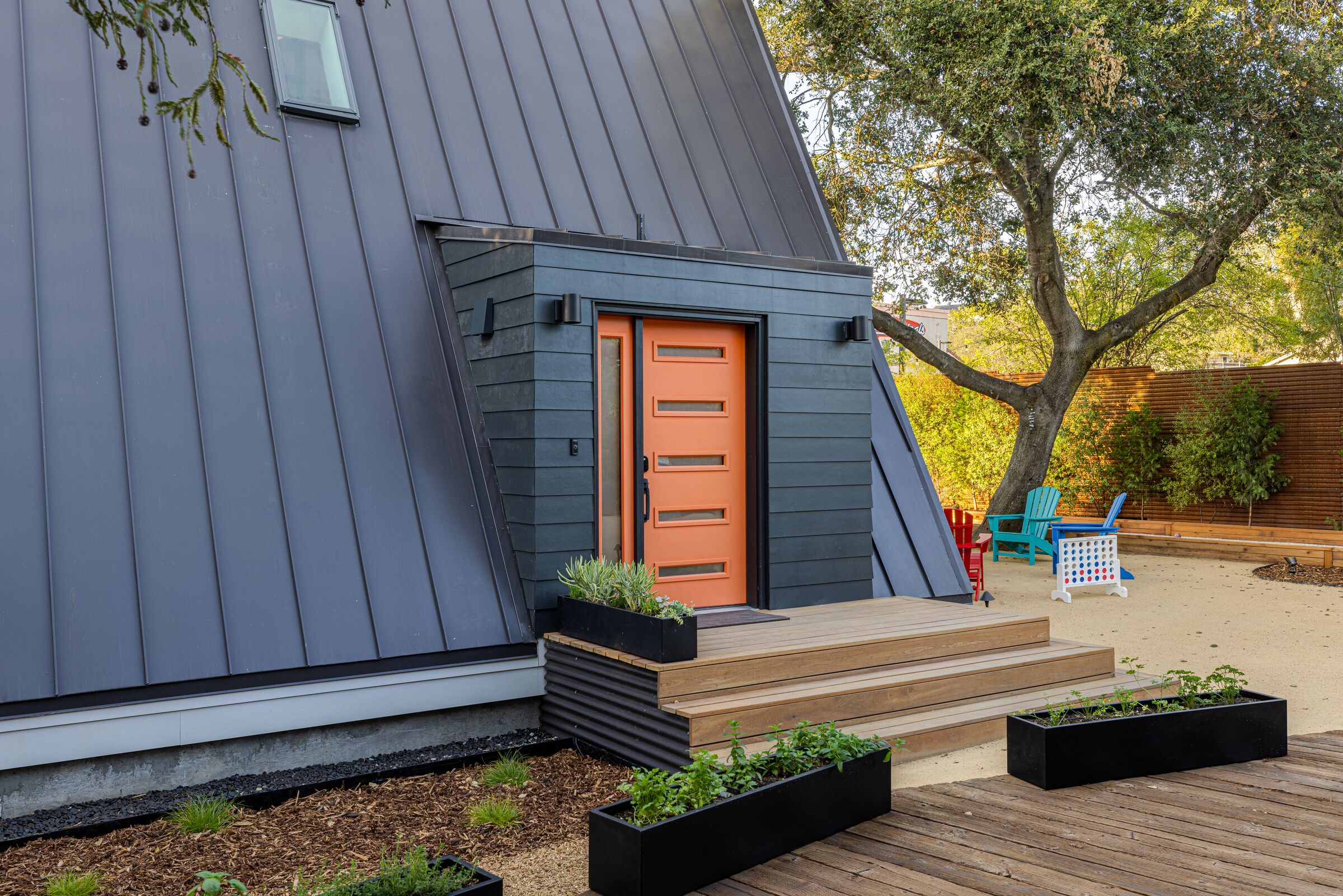 A modern house with a sloped roof, a wooden deck, and a bright orange door.