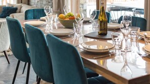 Un coin repas avec une table en bois dressée pour quatre personnes, des chaises de couleur turquoise et un mur en pierre en arrière-plan.