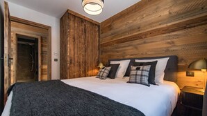Une chambre à coucher avec un grand lit, des lambris en bois sur les murs, une porte et une table de chevet avec une lampe.