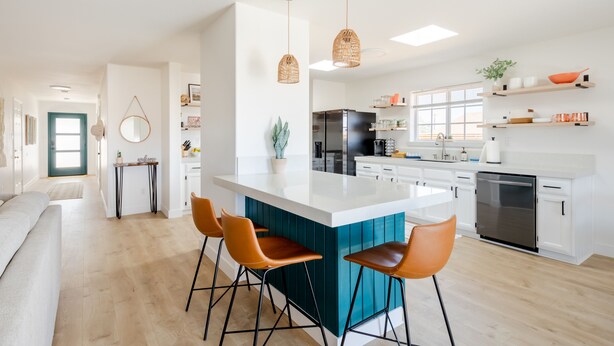Cozinha moderna com ilha central, banquetas, luminárias pendentes e eletrodomésticos embutidos.