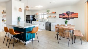 Cozinha moderna com ilha central, banquetas, mesa de jantar com cadeiras e uma obra de arte na parede.