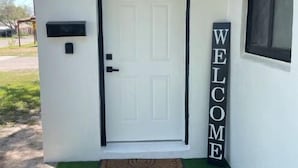 A white exterior with a black door, a welcome sign, a mailbox, and a small window. - Modern 3 Bedroom 2 Bath Home Centrally Located! (Del Rio)