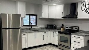A modern kitchen with white cabinets, stainless steel appliances, a wooden floor, and a black dining table. - Modern 3 Bedroom 2 Bath Home Centrally Located! (Del Rio)