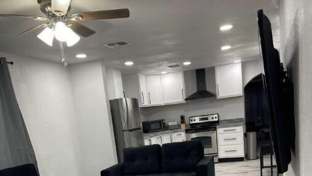 A compact living space with a kitchenette, a ceiling fan, and a dark-colored sofa. - Modern 3 Bedroom 2 Bath Home Centrally Located! (Del Rio)