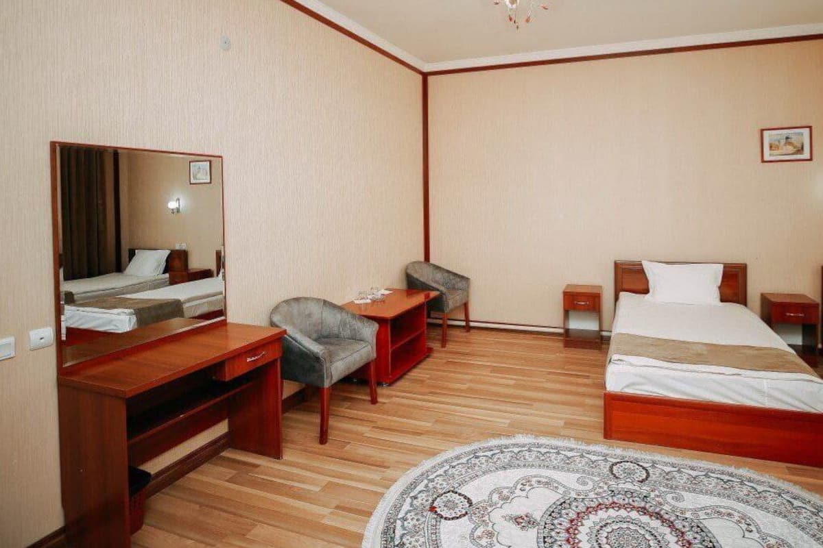 A hotel room with a wooden desk, a chair, a bed, a mirror, and a chandelier.