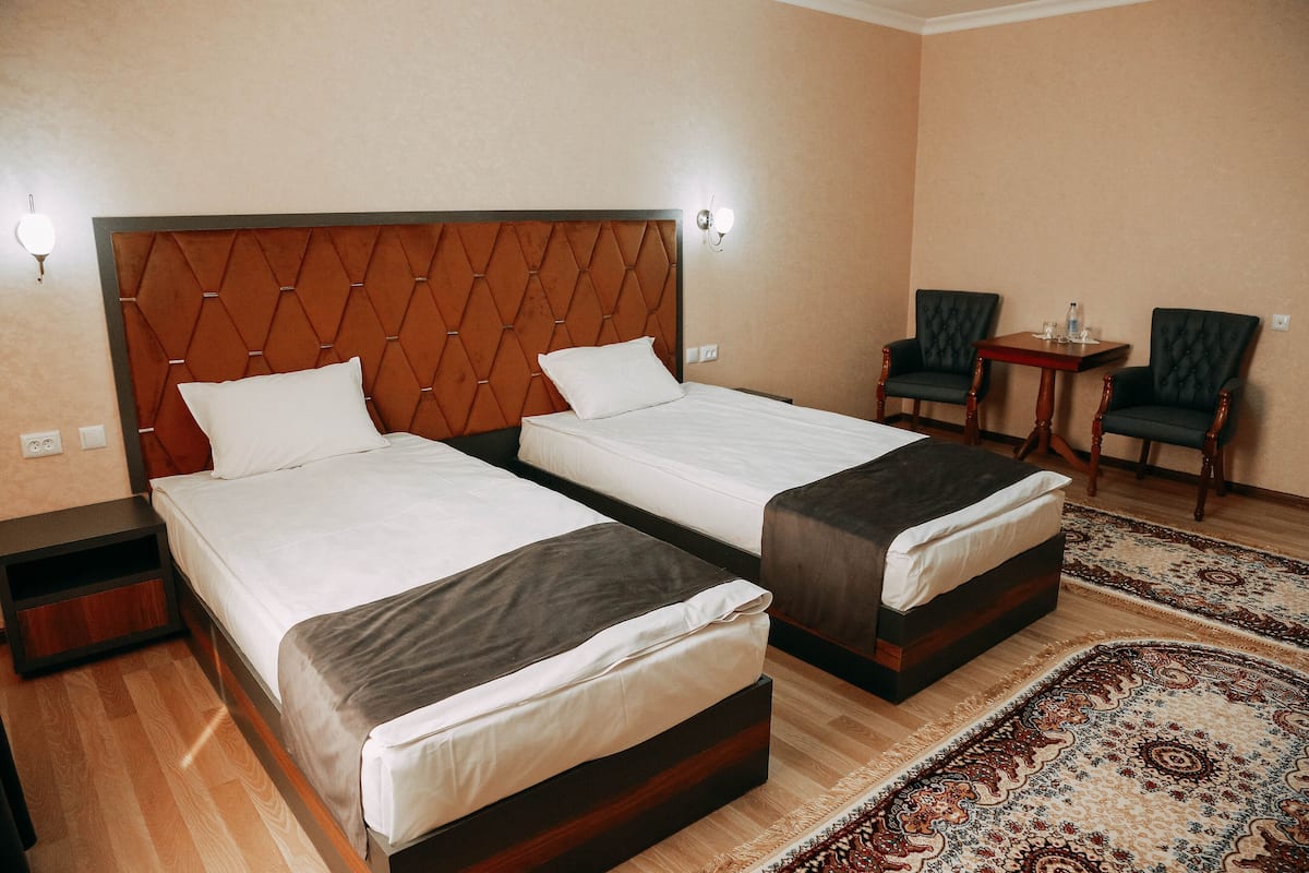 A hotel room with two beds, a small table, two chairs, and a patterned rug.