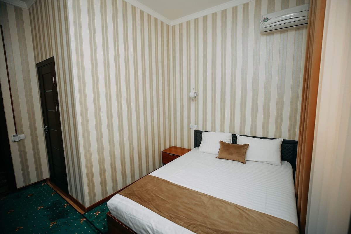 A hotel room with a striped wallpaper, a bed with white and brown bedding, a nightstand, and an air conditioning unit.