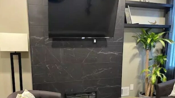 A modern living room with a flat-screen TV mounted on a marble wall, two dark armchairs, a glass coffee table, and a fireplace. - Mr. Holmes Retreat (Pittsburgh)