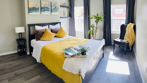 A bedroom with a bed, bedside table, lamp, artwork, curtains, and a view of the outside. - Mr. Holmes Retreat (Pittsburgh)