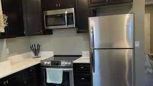 A modern kitchen with dark cabinets, stainless steel appliances, and a white countertop. - Mr. Holmes Retreat (Pittsburgh)