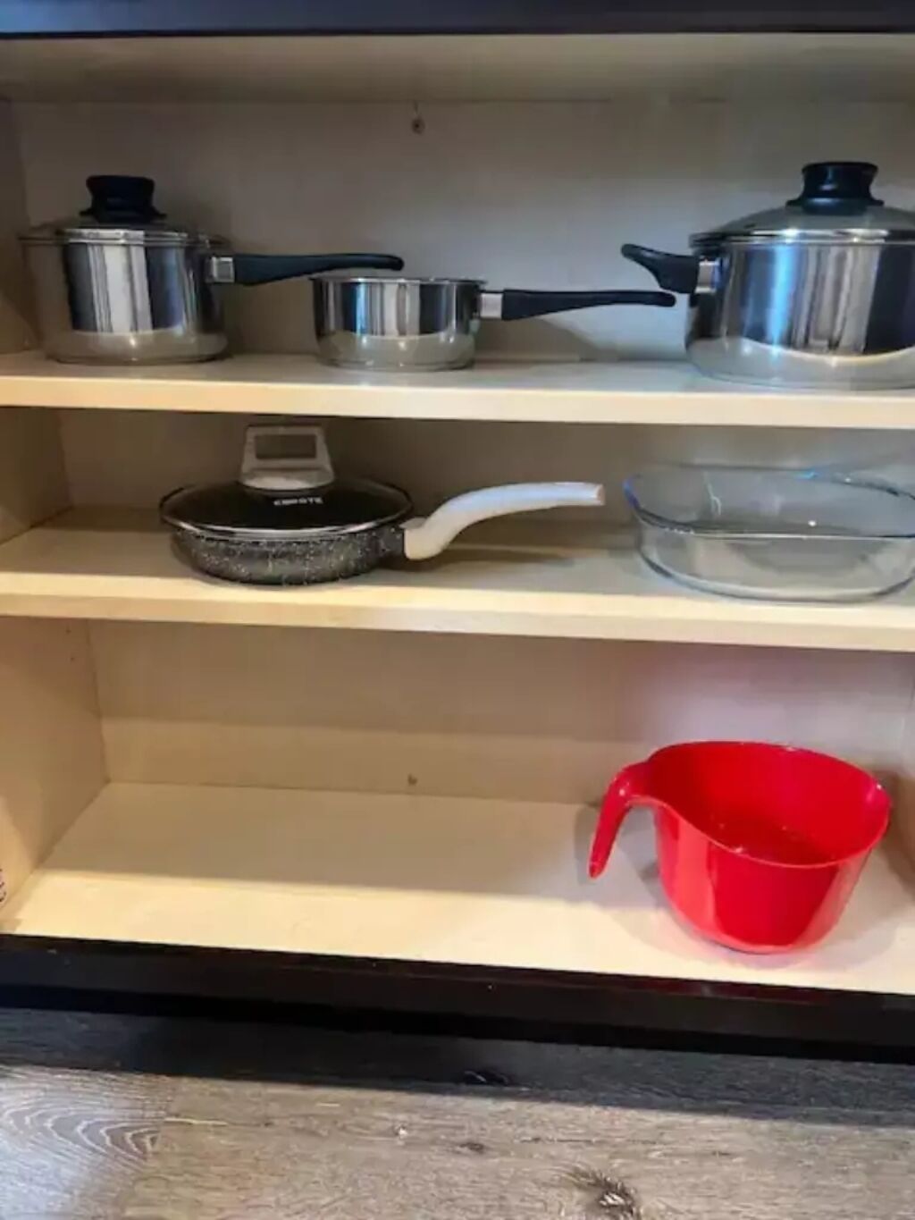 Une étagère de cuisine avec des ustensiles de cuisine et un verre doseur rouge.