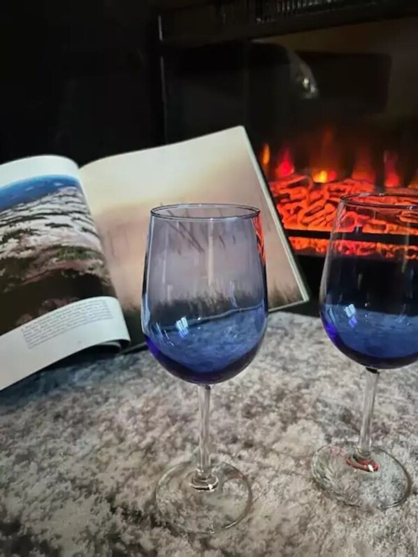 Two wine glasses on a marble surface with an open book and a fireplace in the background.